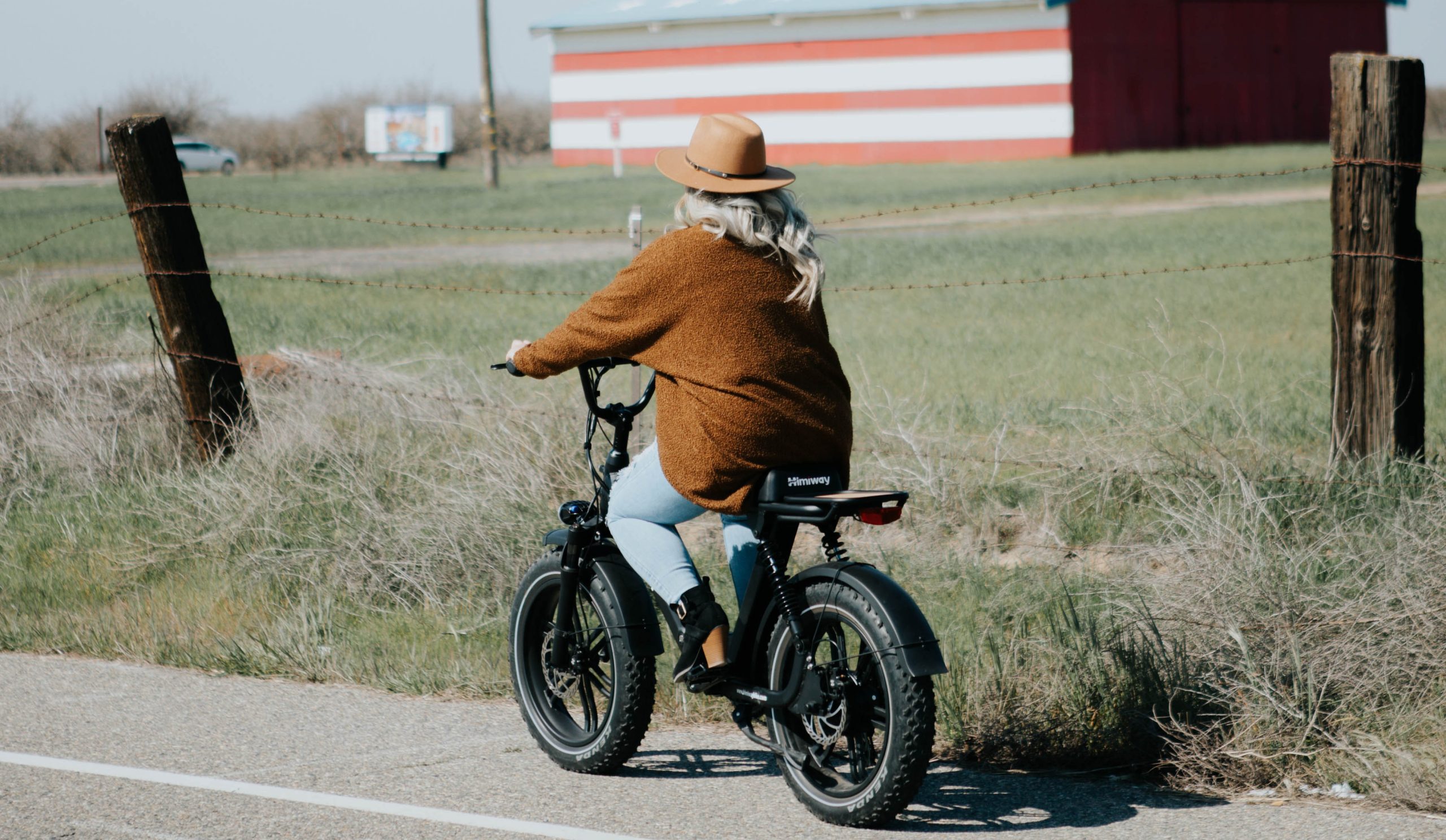 older lady riding an electric bike along a country road next to a farm