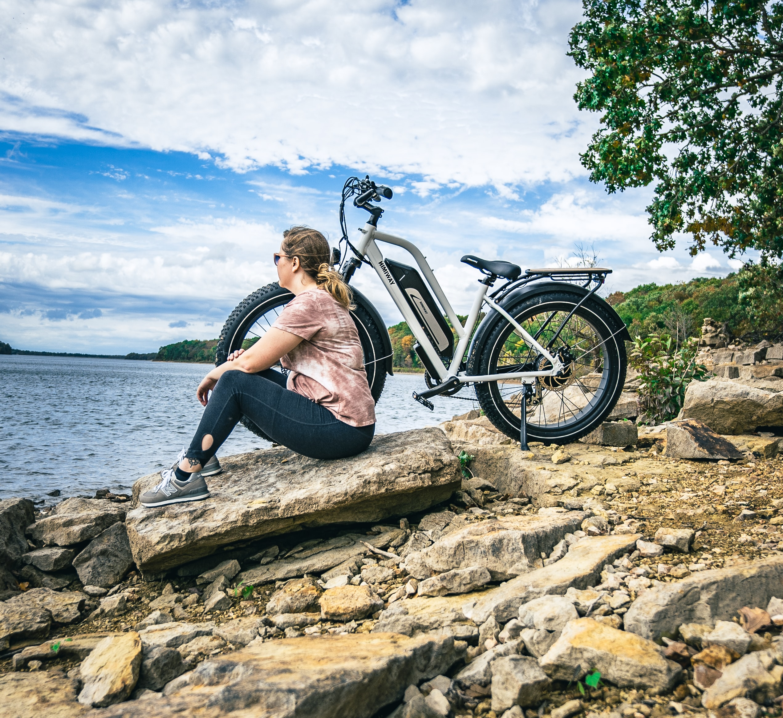 woman sitting beside her step-through electric bike on the beach at a lake