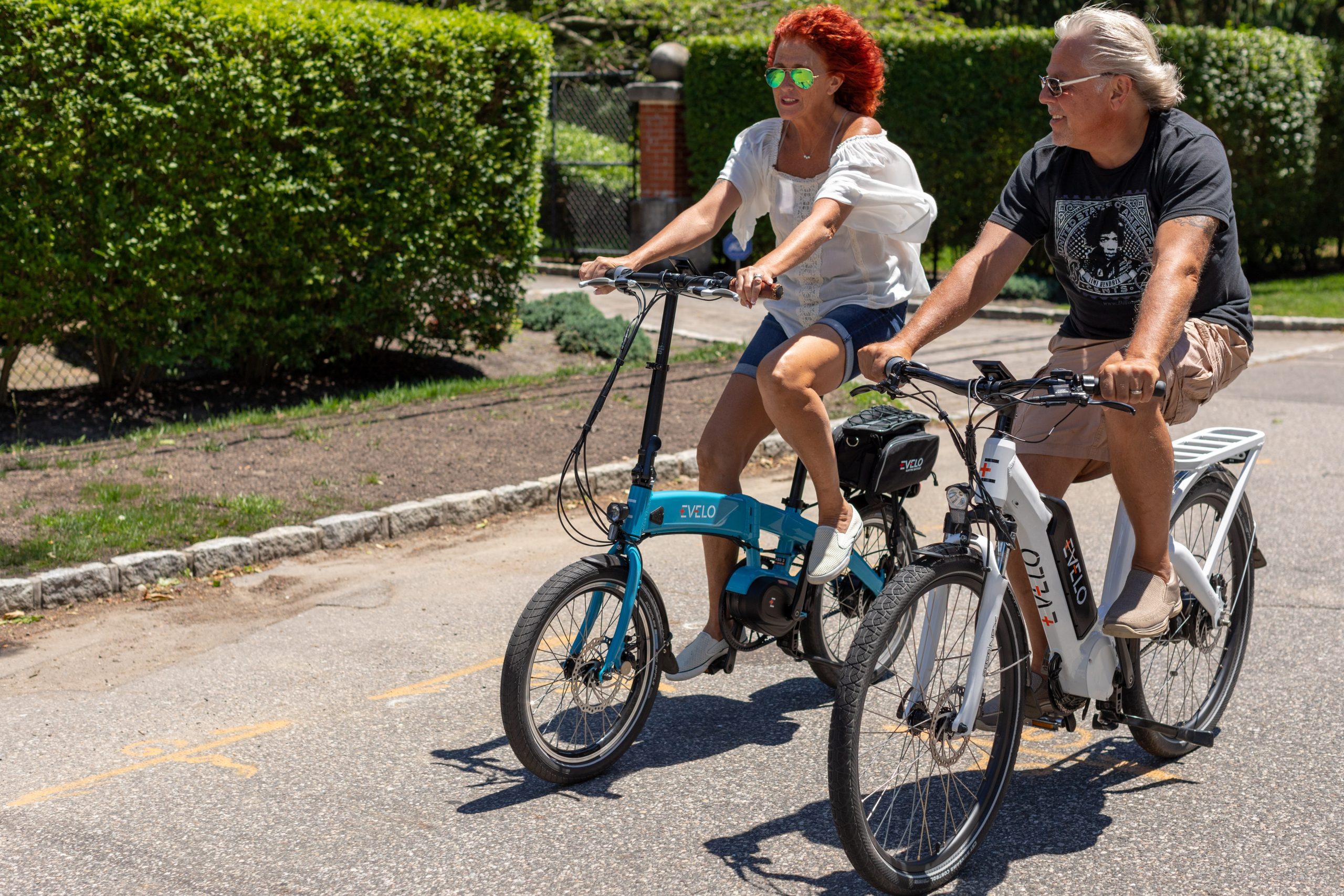 older couple riding their electric bikes down a suburban neighborhood road